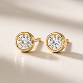 Gold diamond stud earrings on a beige background