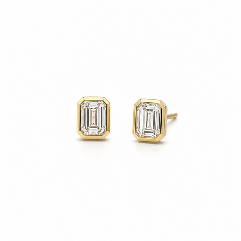 bezel setting emerald cut diamond earrings on white background.